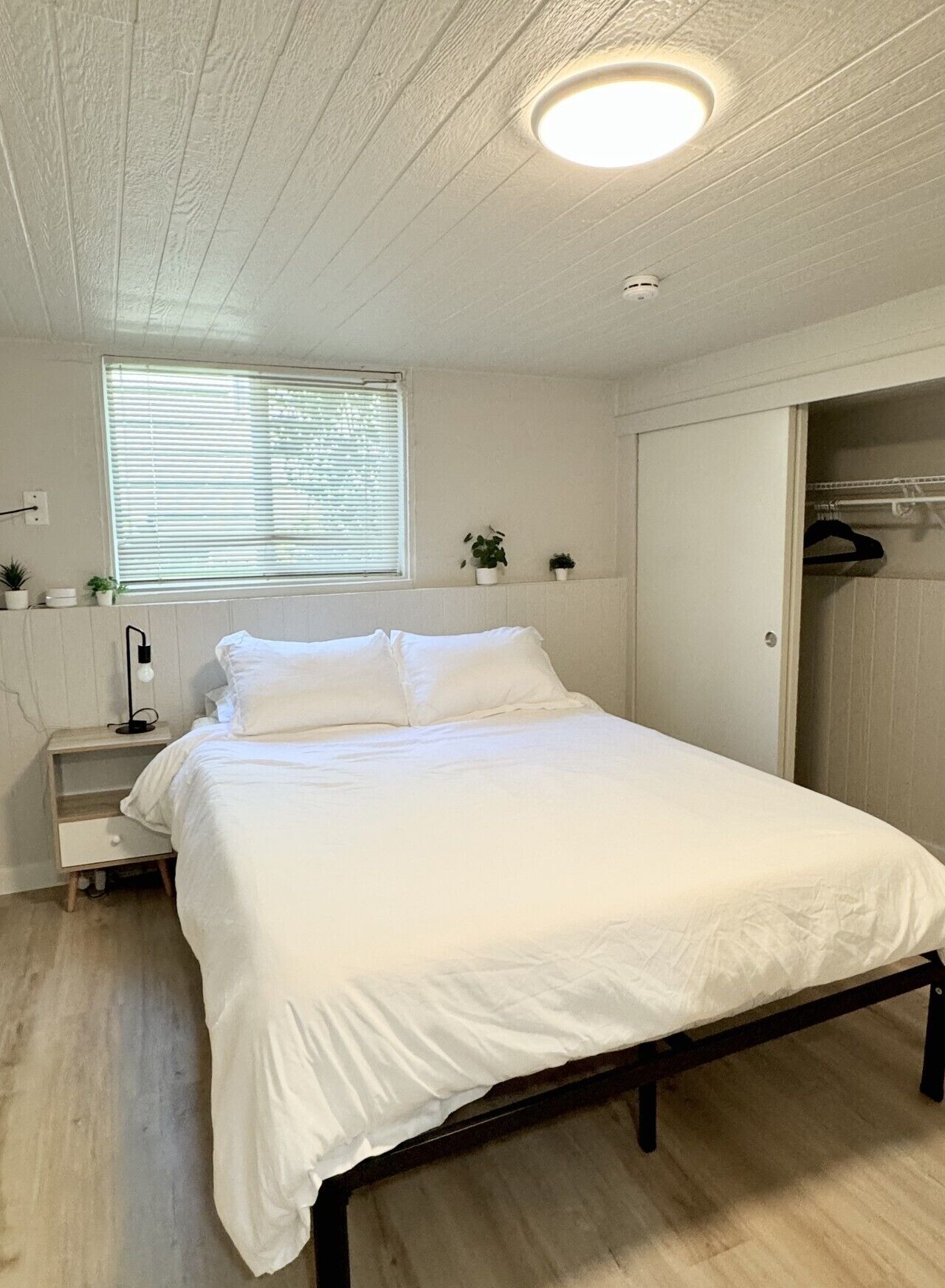 Un dormitorio con cama, mesita de noche, lámpara, ventana y armario.