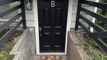 Una porta nera con la lettera 'B' sopra, una scala in cemento che conduce alla porta e un tappetino colorato con la scritta 'hello'.