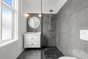 A modern bathroom with a white vanity, a round mirror, a shower, and a view of the sky through a window. - Rare gem! 3BR/3BA Downtown Apartment in Reykjavik (Reykjavík)
