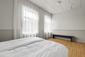 A minimalist bedroom with a large bed, a bench, and sheer curtains. - Rare gem! 3BR/3BA Downtown Apartment in Reykjavik (Reykjavík)