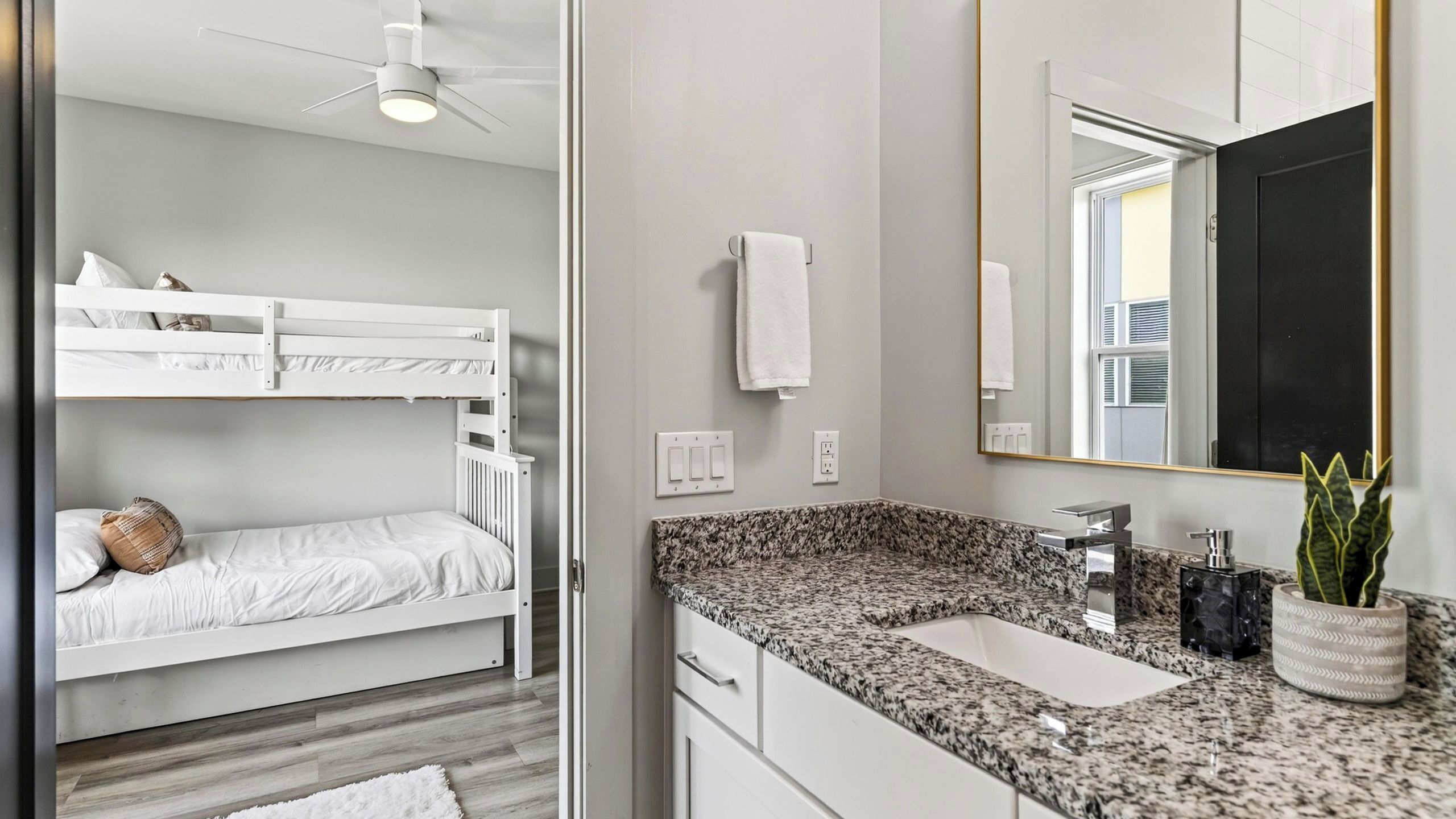 Une chambre moderne avec des lits superposés, une salle de bain dotée d’un comptoir en granit et d’un grand miroir.
