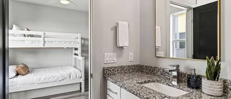 Une chambre moderne avec des lits superposés, une salle de bain dotée d’un comptoir en granit et d’un grand miroir.