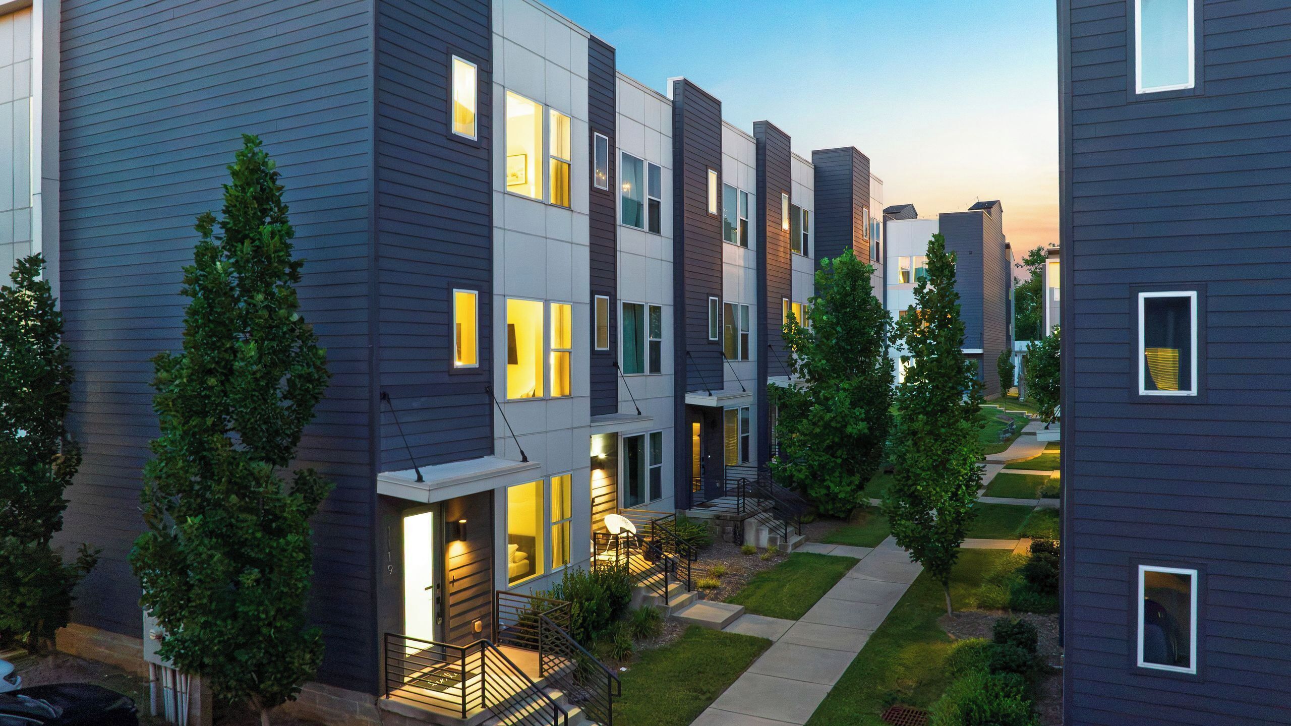 A modern multi-story residential building with a well-maintained lawn and a clear sky.
