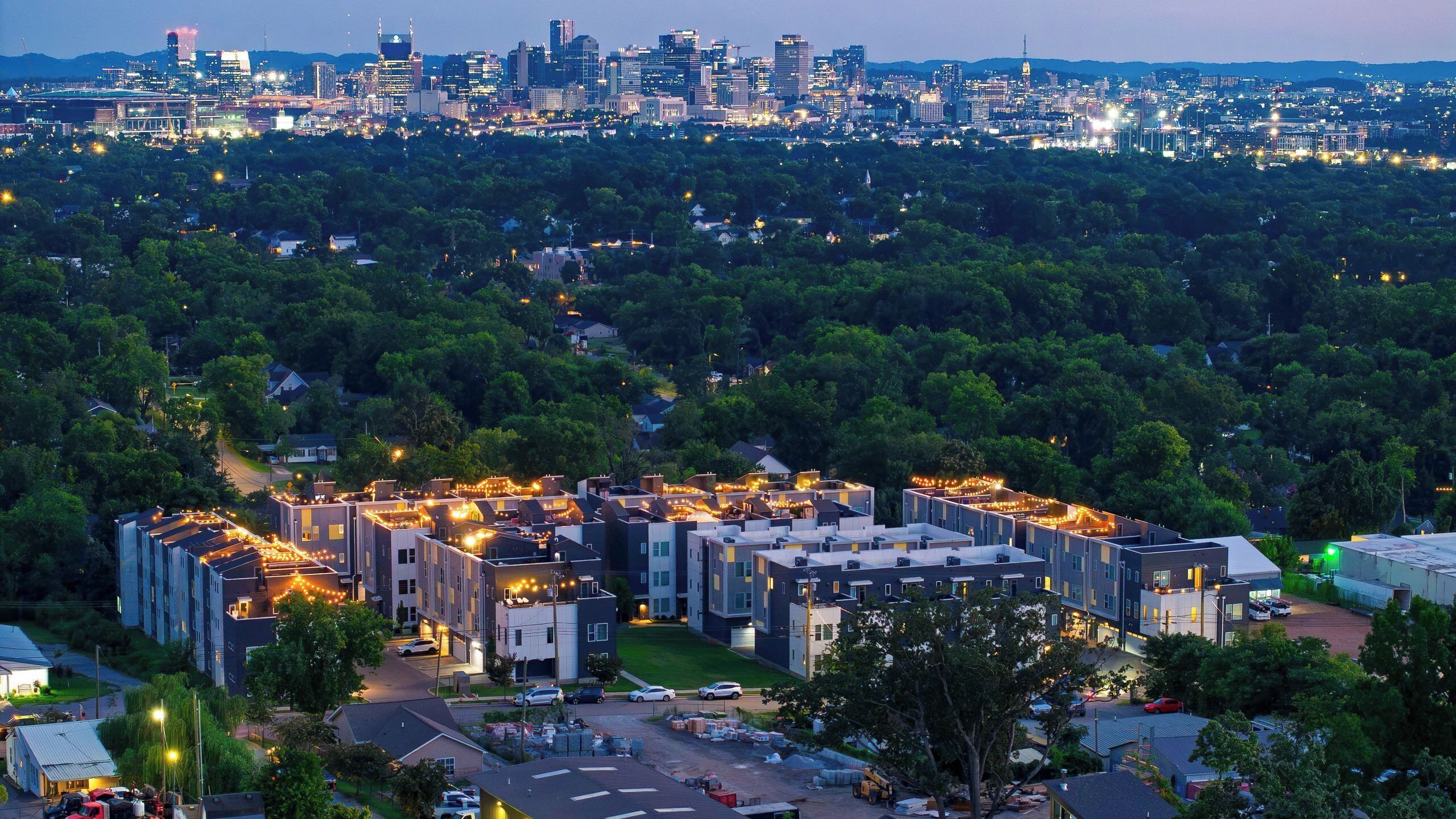 A residential area with modern apartment buildings, a parking lot, and a distant city skyline.