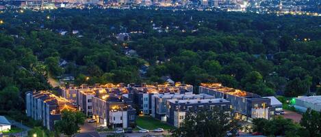 A residential area with modern apartment buildings, a parking lot, and a distant city skyline.