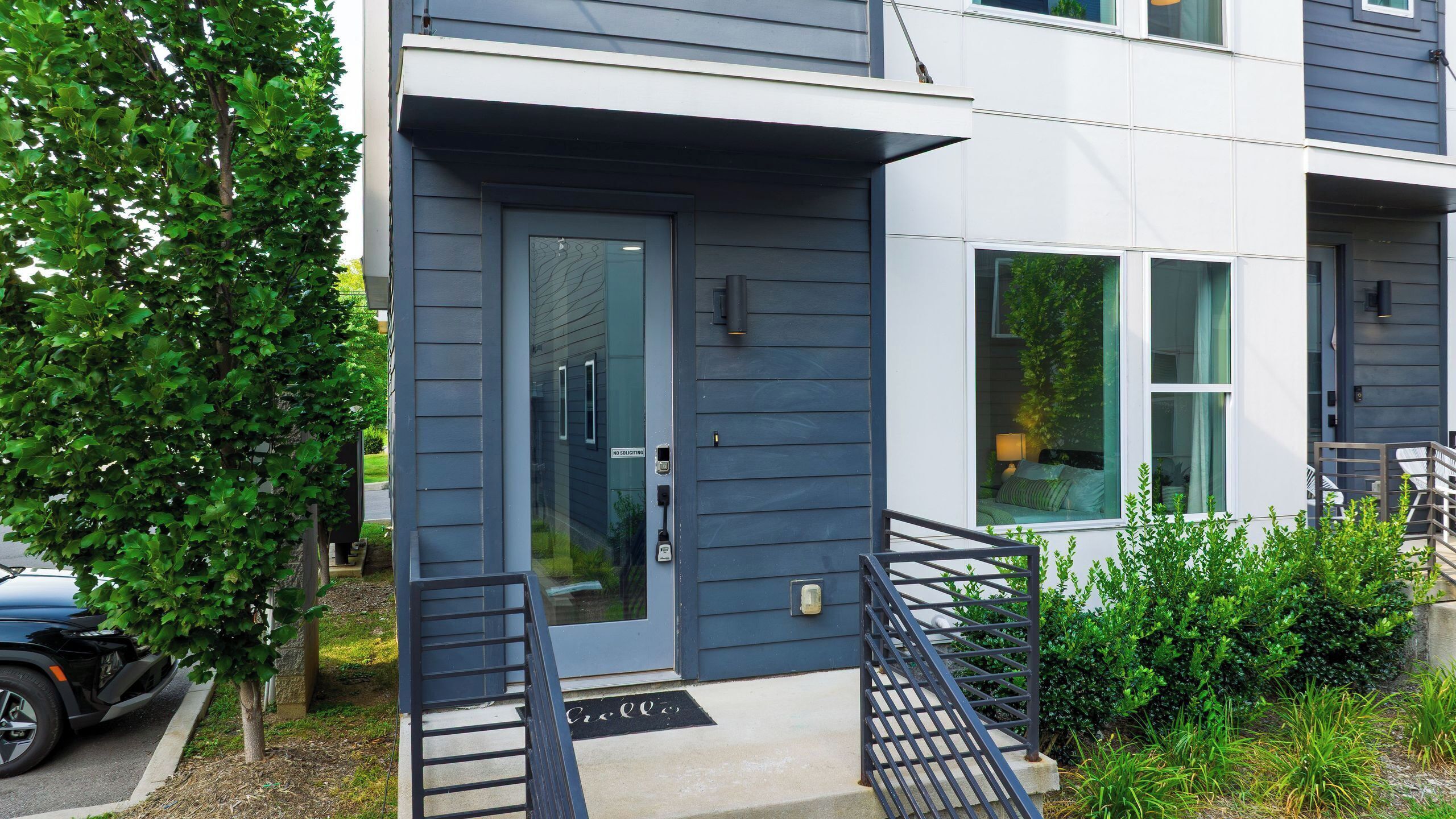 A modern two-story building with a dark blue exterior, a front door with a glass panel, and a small porch with a metal railing.