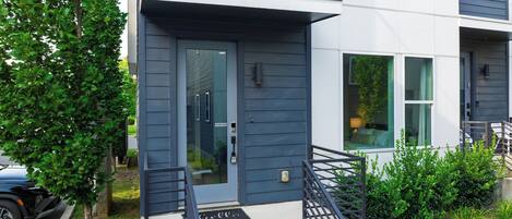 A modern two-story building with a dark blue exterior, a front door with a glass panel, and a small porch with a metal railing.