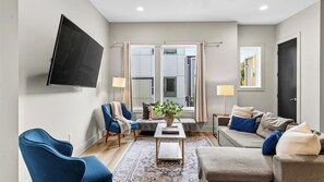 A modern living room with a flat-screen TV, blue armchairs, a grey sofa, and a coffee table with a plant. - Harmony House by Avantstay Sunlit Open Design + Island Kitchen Five Points + Broadway (Nashville)