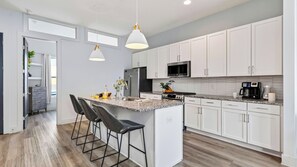 A modern kitchen with white cabinets, a granite countertop, and a central island with bar stools. - Harmony House by Avantstay Sunlit Open Design + Island Kitchen Five Points + Broadway (Nashville)