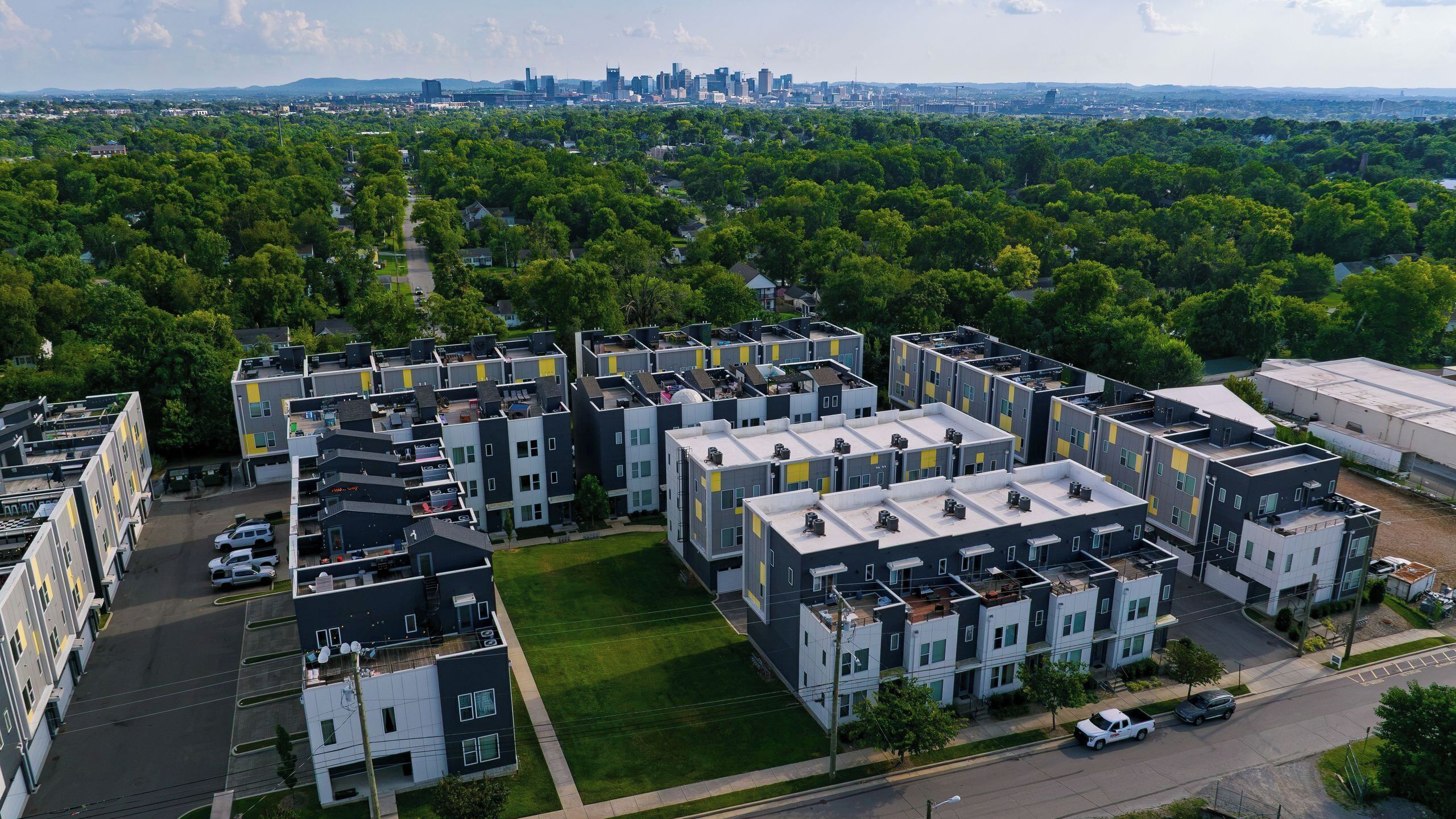 Un complexe d’appartements moderne composé de plusieurs immeubles, doté d’un espace vert central et offrant une vue sur les contours d’une ville lointaine.