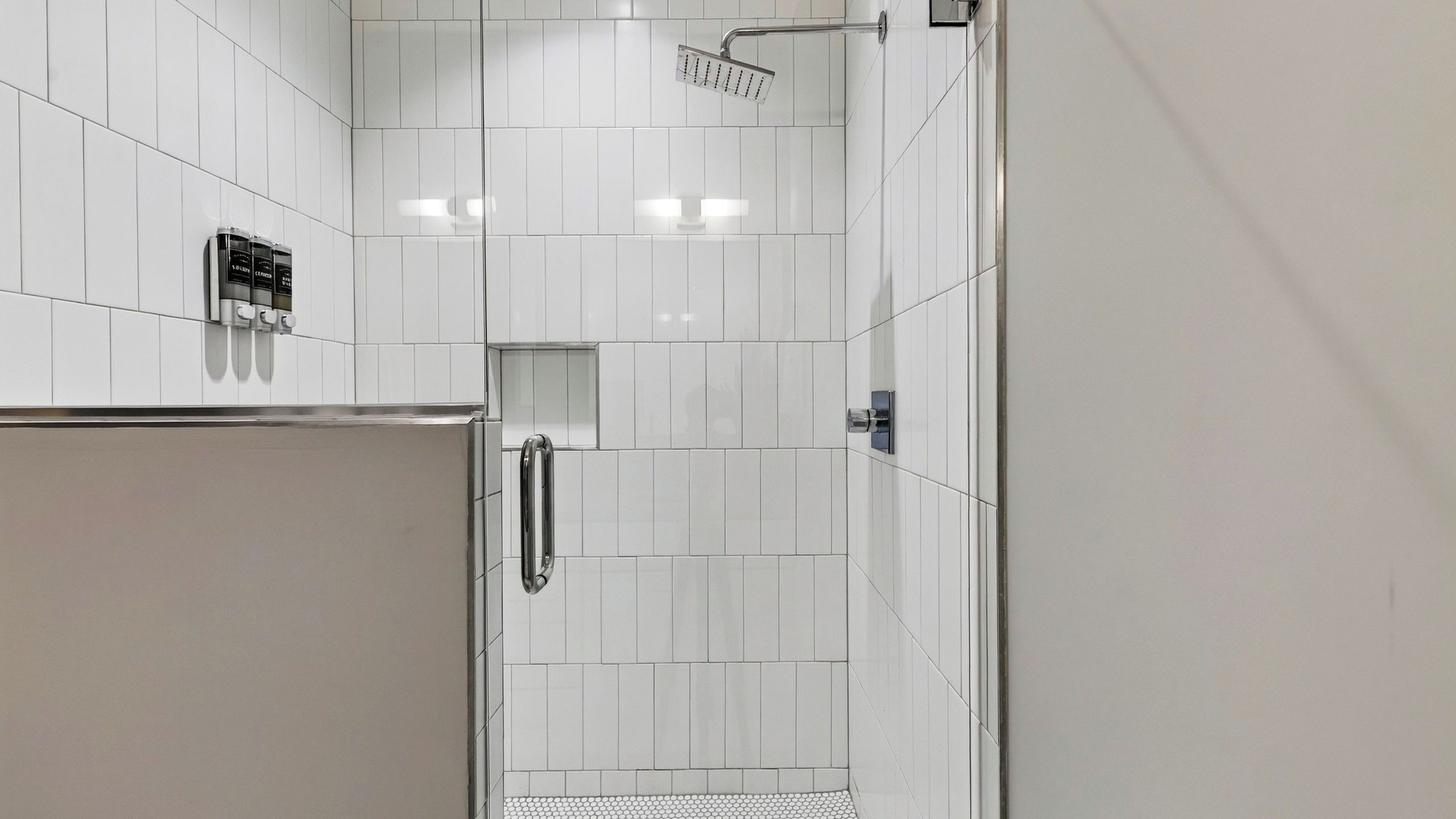 Casa de banho moderna com azulejos brancos, chuveiro e sanita embutida.