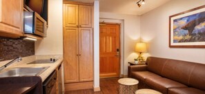 A kitchen with wooden cabinets, a stainless steel sink, and a countertop. There is a brown leather sofa and a small round table with a lamp. - Westgate 1BR ski-in/out at the Canyons Village. Pools, Hot Tubs, Ski Valet &more (Park City)
