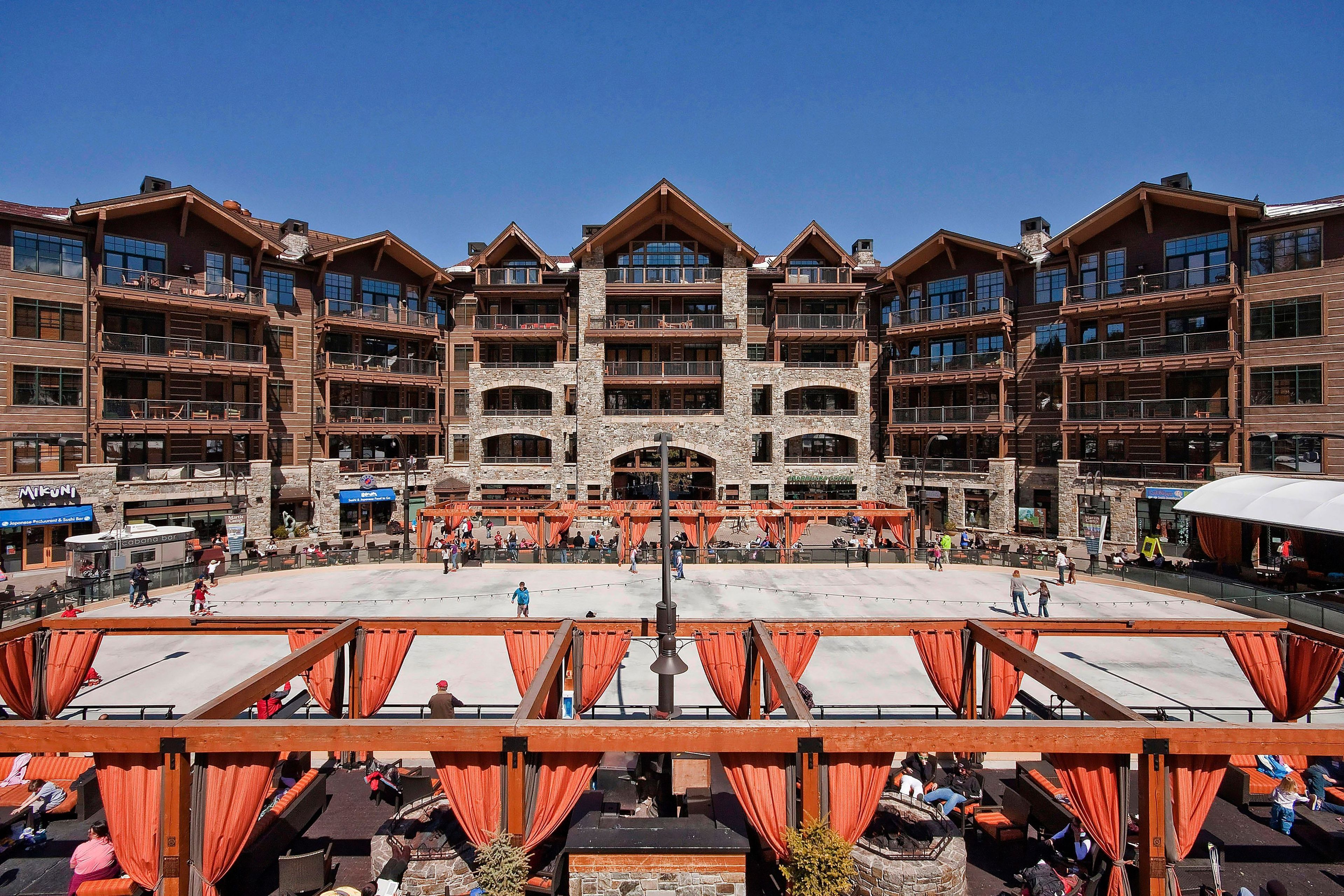 A multi-story hotel with a central courtyard, outdoor seating, and a ski slope in the background.