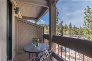 A covered outdoor area with a table and chairs, a potted plant, and a view of a snowy landscape and trees. - Northstar Village Condo (Truckee)