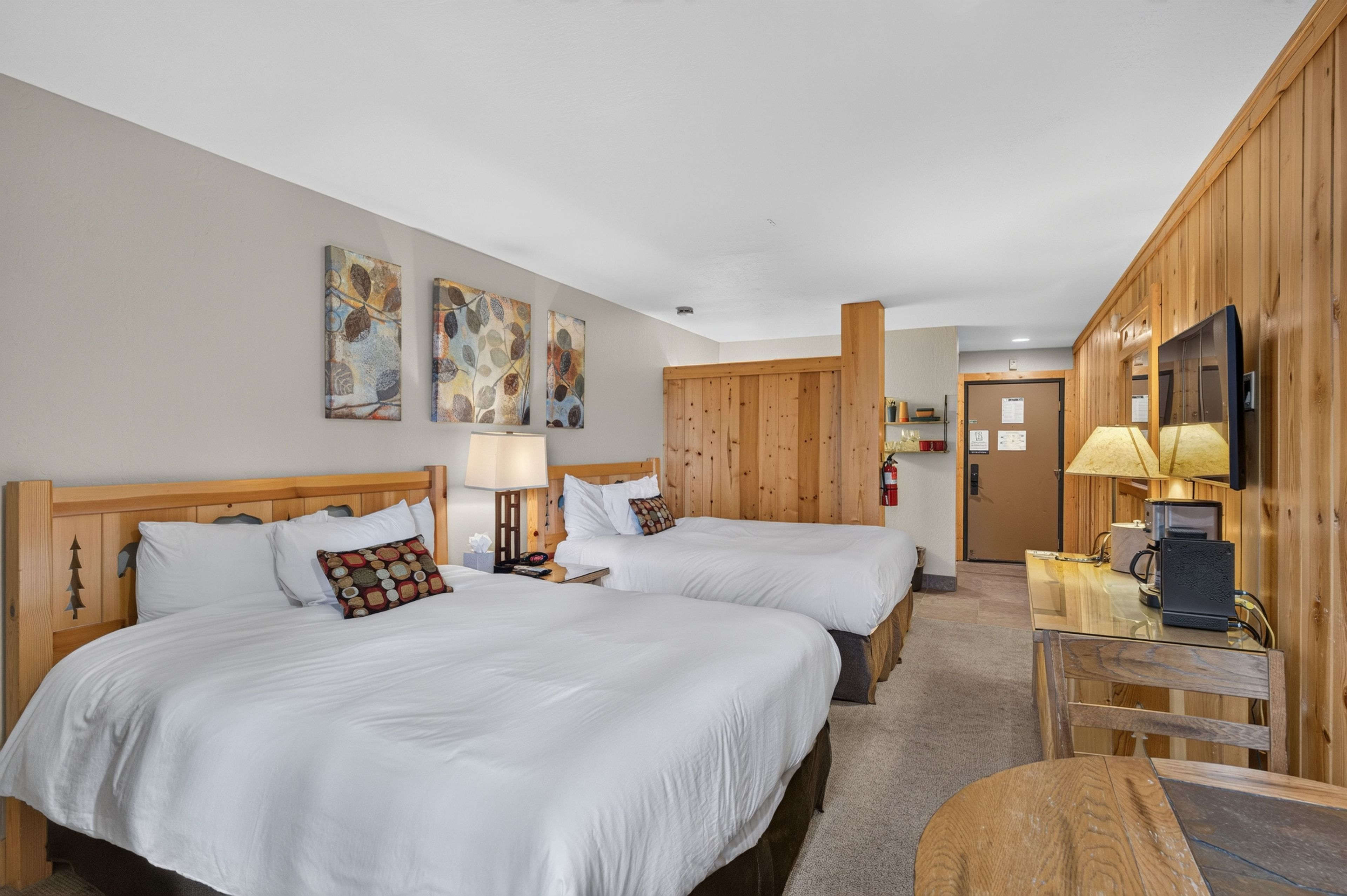 Une chambre d ’hôtel avec deux lits, une tête de lit en bois, un bureau avec une lampe et un téléviseur.