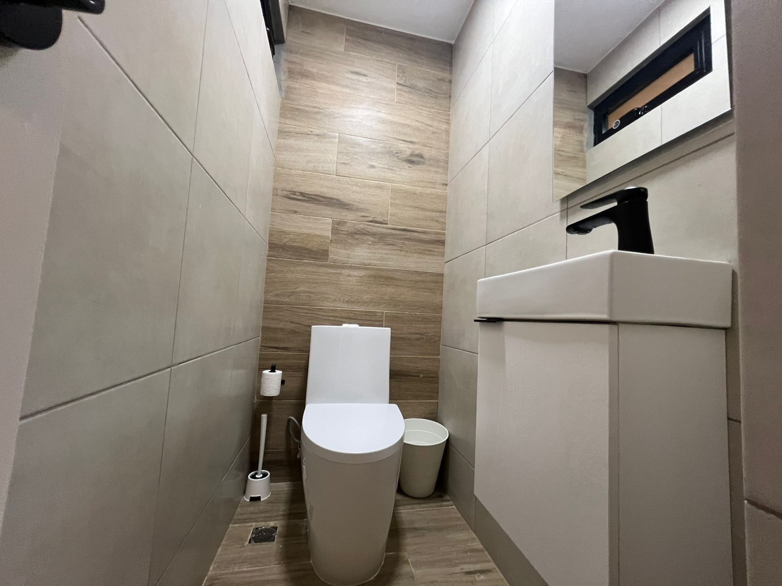 Ein kleines Badezimmer mit Toilette, Mülleimer und einem wandmontierten Waschbecken.