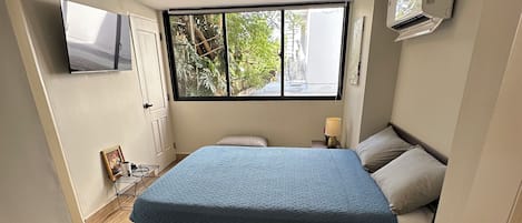 A bedroom with a bed, a window, a TV, and an air conditioning unit.