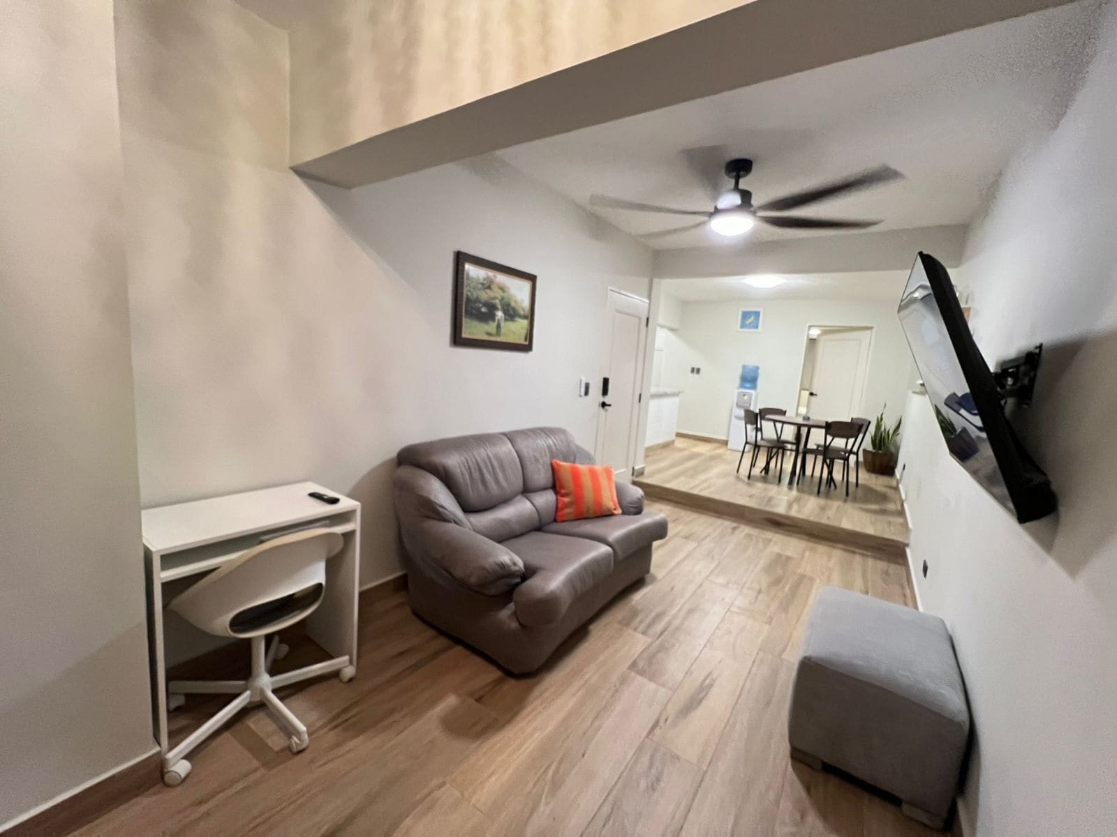 A modern living room with a leather sofa, a white desk, and a ceiling fan.