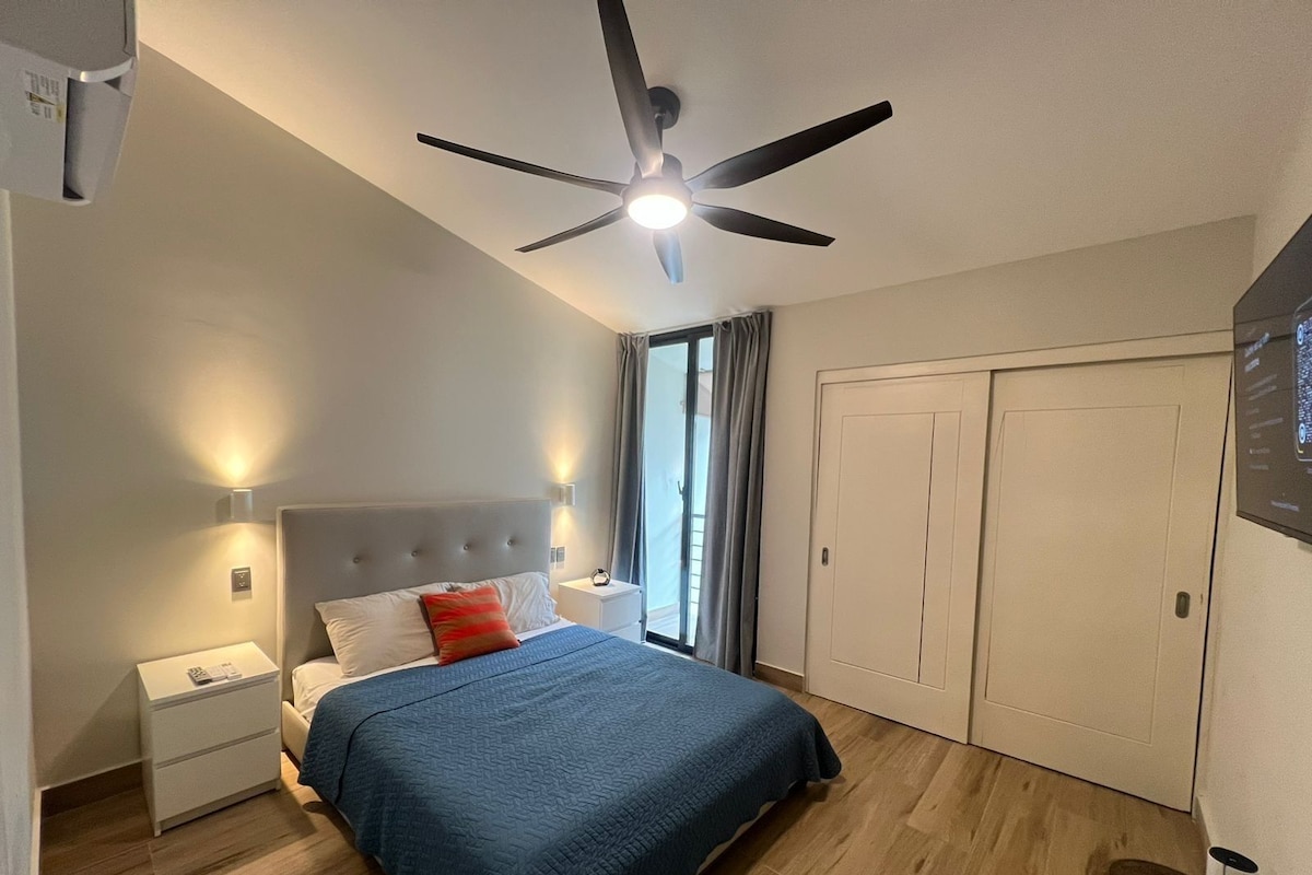Ein Hotelzimmer mit Bett, Nachttischen, Deckenventilator, Kleiderschrank und einem fenster mit Vorhängen.