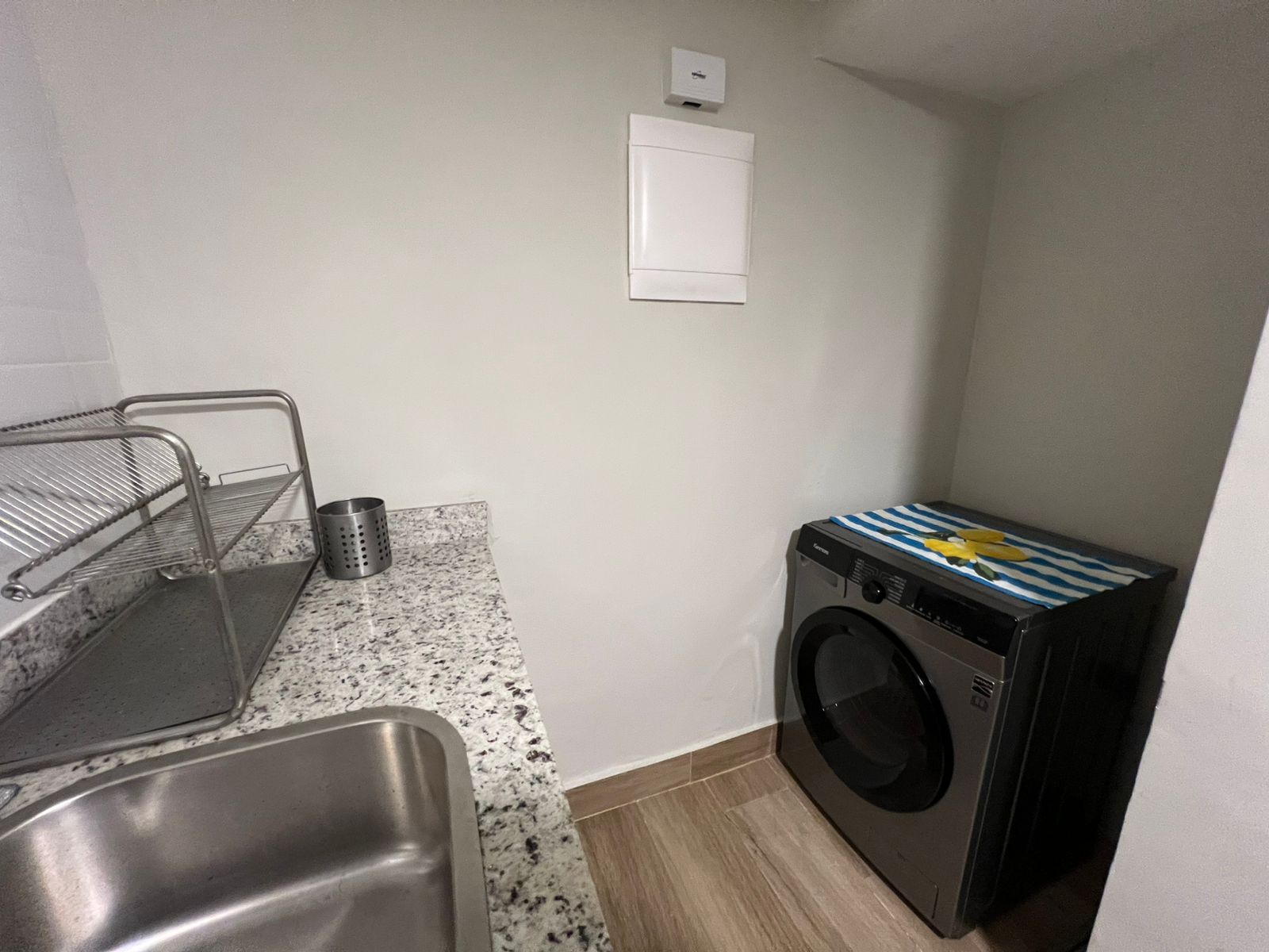 Cocina compacta con pileta, un escurreplatos metálico, lavadora y una pequeña mesada.
