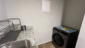 Cocina compacta con pileta, un escurreplatos metálico, lavadora y una pequeña mesada.