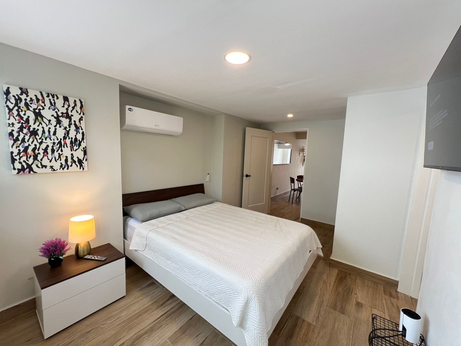 Ein Schlafzimmer mit einem Bett, einem Nachttisch, einer Lampe und einer Wand-Klimaanlage.