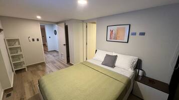 Quarto de hotel com cama, mesa de cabeceira, obra de arte na parede e porta que dá para outro cômodo.