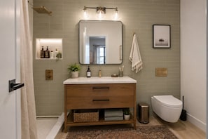A bathroom with a wooden vanity, a mirror, a towel rack, a toilet, and a shower area. - Spacious Apartment Near Times Square (New York)