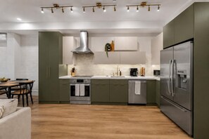 A modern kitchen with a built-in oven, a stainless steel refrigerator, and a dining area with a wooden table and chairs. - Spacious Apartment Near Times Square (New York)
