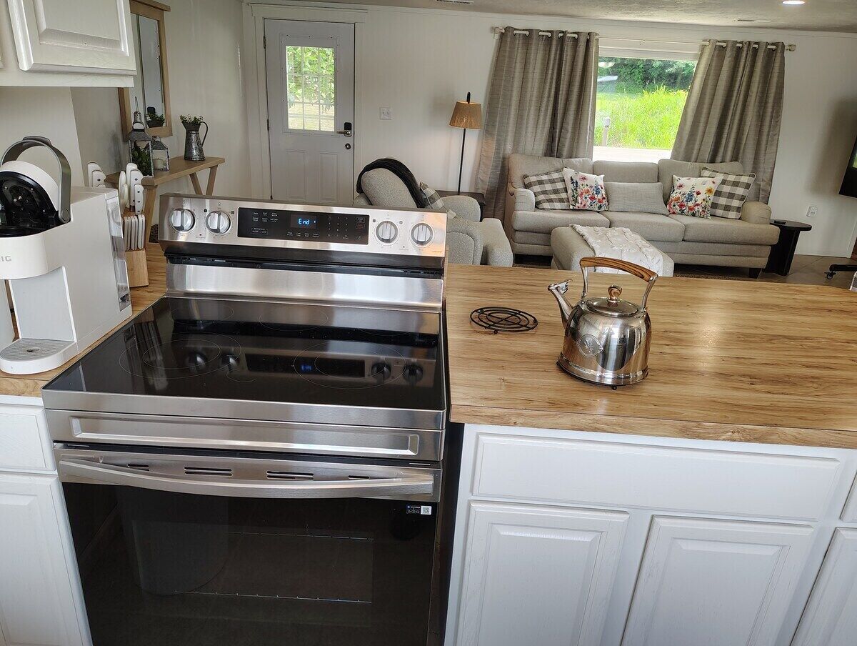 A kitchen with a stainless steel stove, a wooden countertop, and a kettle.