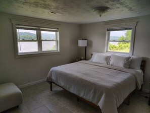 A bedroom with a bed, two windows, a nightstand, and a lamp.
