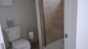 Casa de banho com sanita, chuveiro com porta de vidro e barra de toalhas.