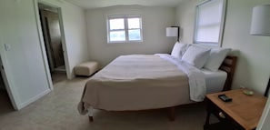 Un dormitorio con una cama, una mesita de noche, una ventana y una puerta.