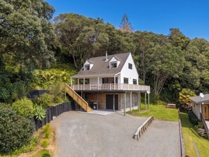 A two-story house with a balcony, surrounded by dense greenery. - Skippers View - Onemana Holiday Home (Whangamata)