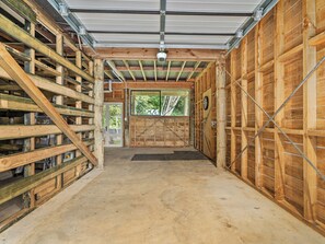 A covered wooden structure with a concrete floor, metal beams, and a door leading to an outdoor area. - Skippers View - Onemana Holiday Home (Whangamata)