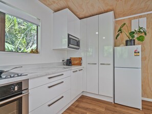 A modern kitchen with white cabinetry, a built-in microwave, and a refrigerator. - Skippers View - Onemana Holiday Home (Whangamata)