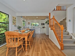 A modern kitchen with white cabinets, a wooden dining table, and a staircase with wooden railings. - Skippers View - Onemana Holiday Home (Whangamata)