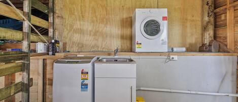 A laundry area with a washing machine and two dryers, wooden walls, and a concrete floor.
