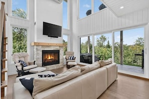 Ein modernes Wohnzimmer mit Kamin aus Stein, einer Ledersofa und einem großen Fenster mit Blick ins Freie.