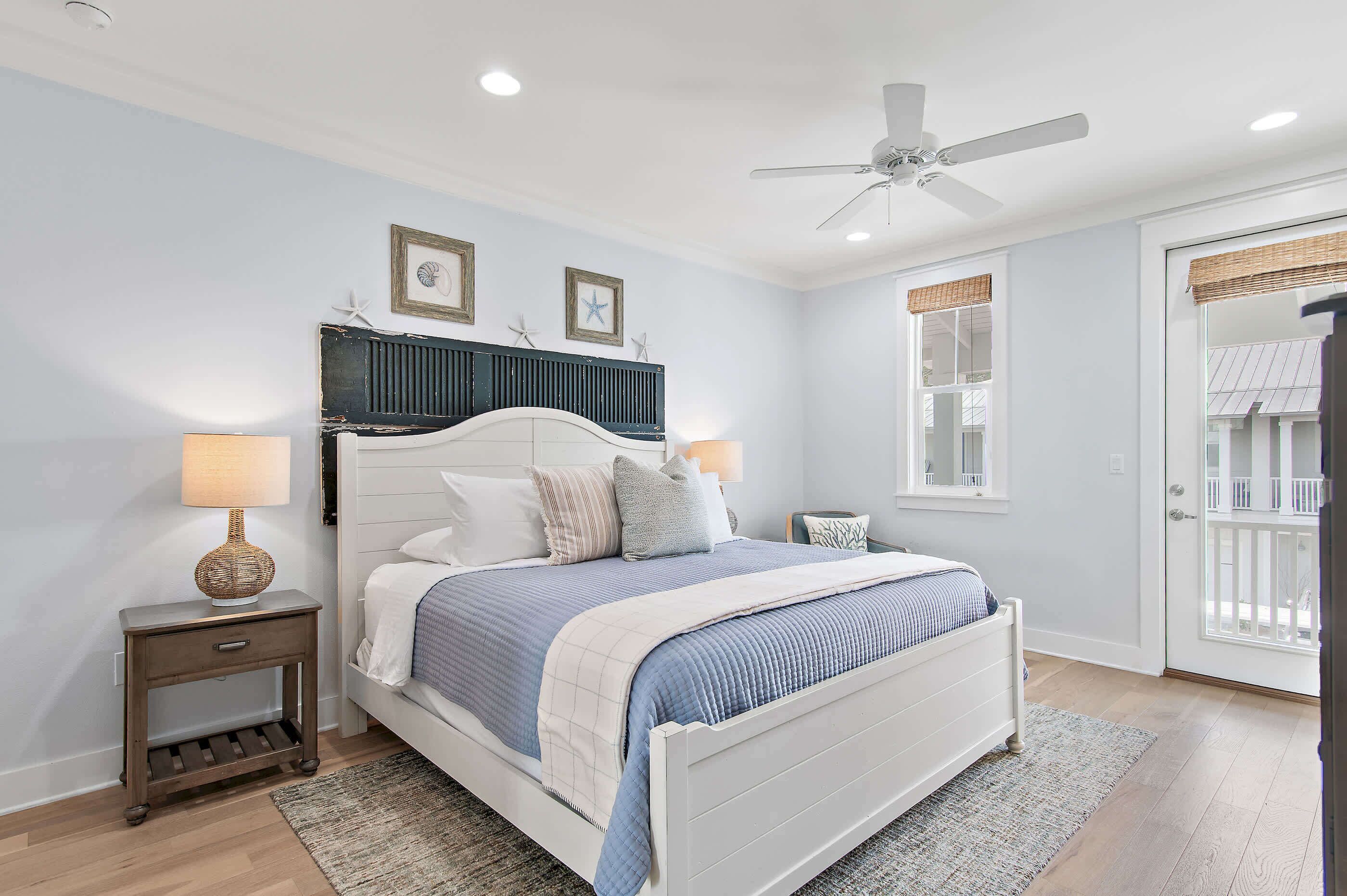A bedroom with a bed, nightstands, a ceiling fan, a window with a view, and a door.