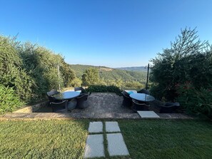 An outdoor seating area with two round tables and chairs, surrounded by lush greenery and a view of distant hills. - Private Tuscan Wine Estate with 3 Houses and Sweeping Views of the Chianti Hills (Toscana)