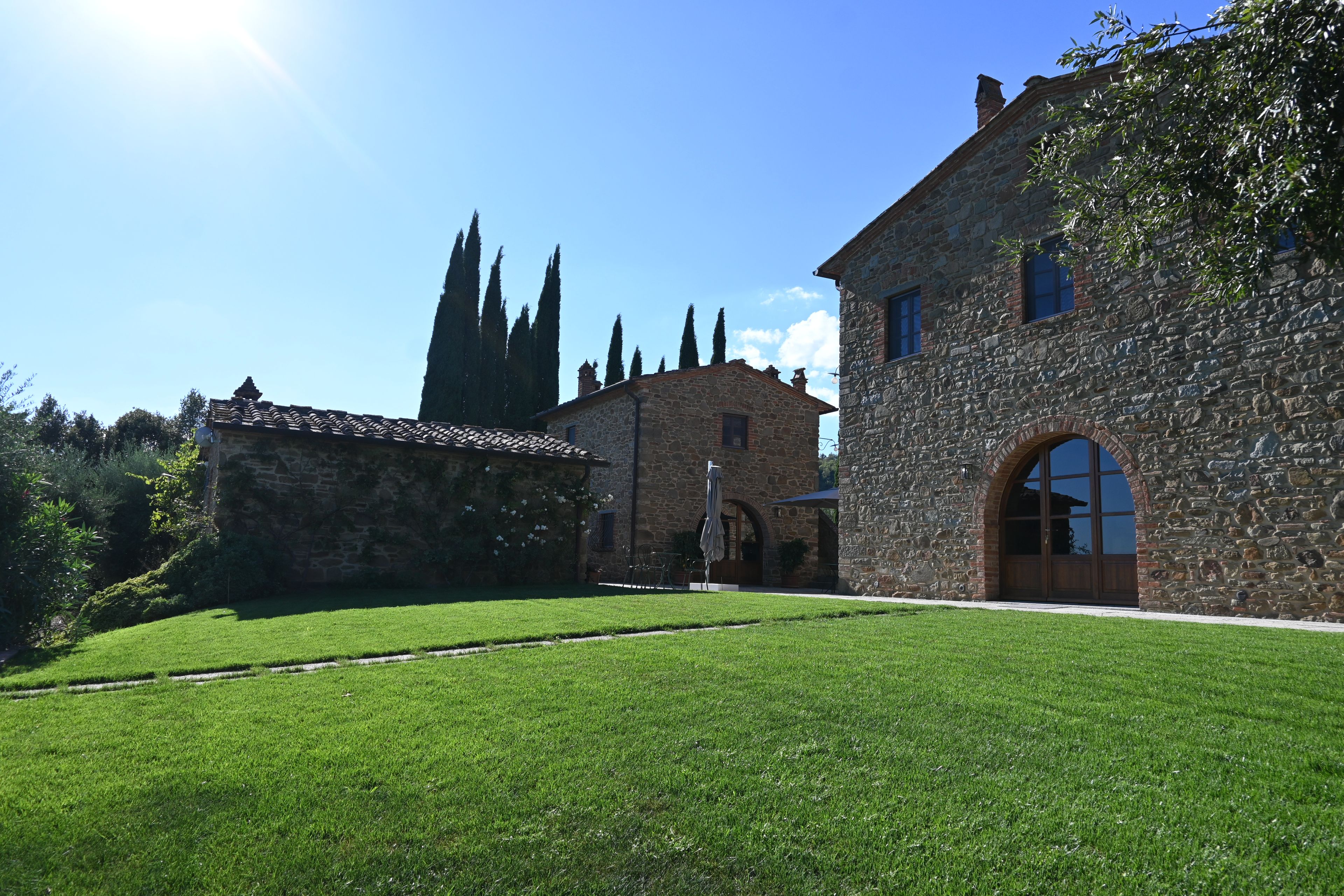 A stone building with a large arched entrance, a well-maintained lawn, and a clear blue sky.