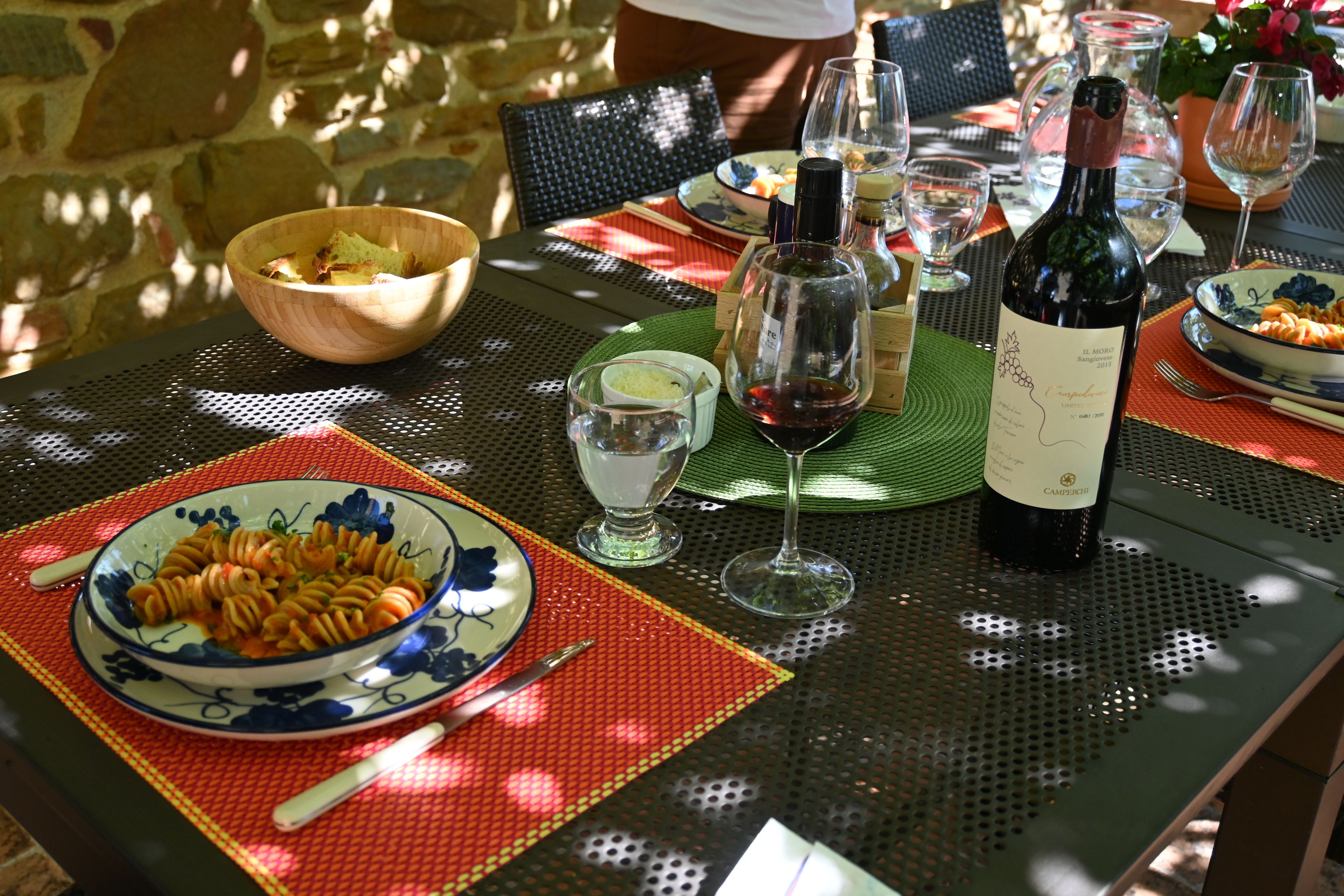 Mesa posta para refeição com pratos de massa, copos de vinho e uma garrafa de vinho.