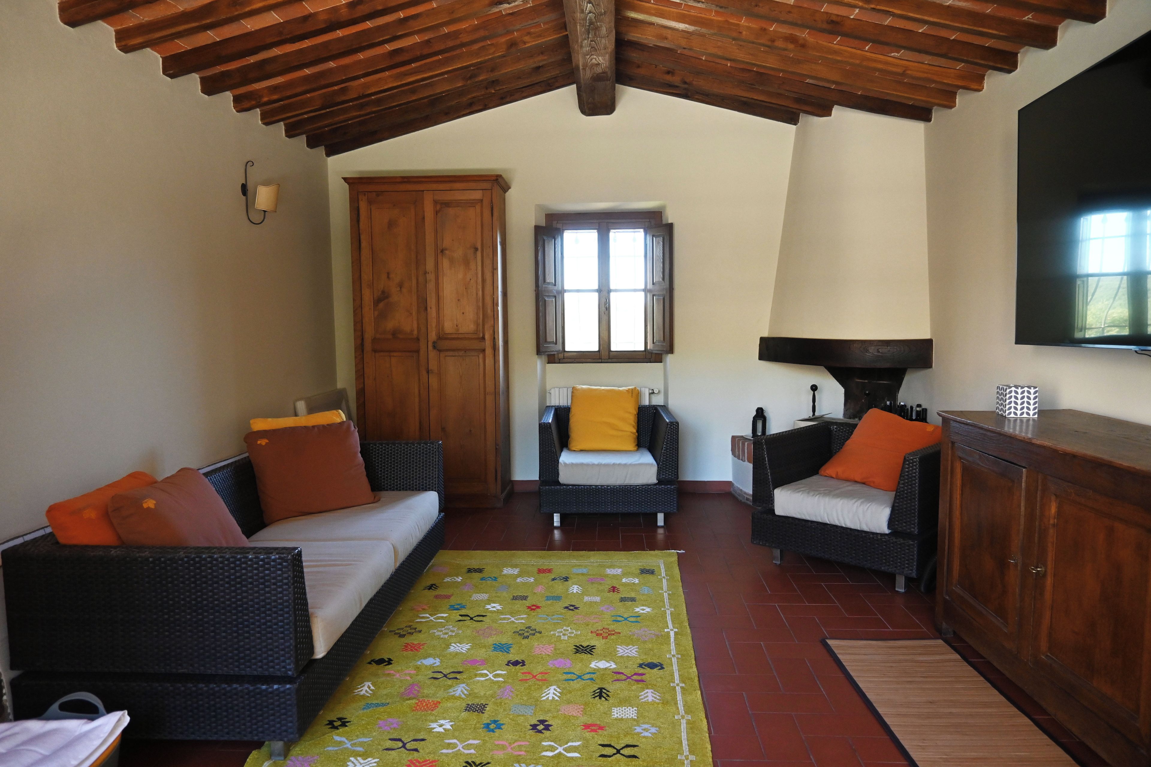 A cozy living room with a high wooden ceiling, a sofa, two armchairs, a small table, and a television.