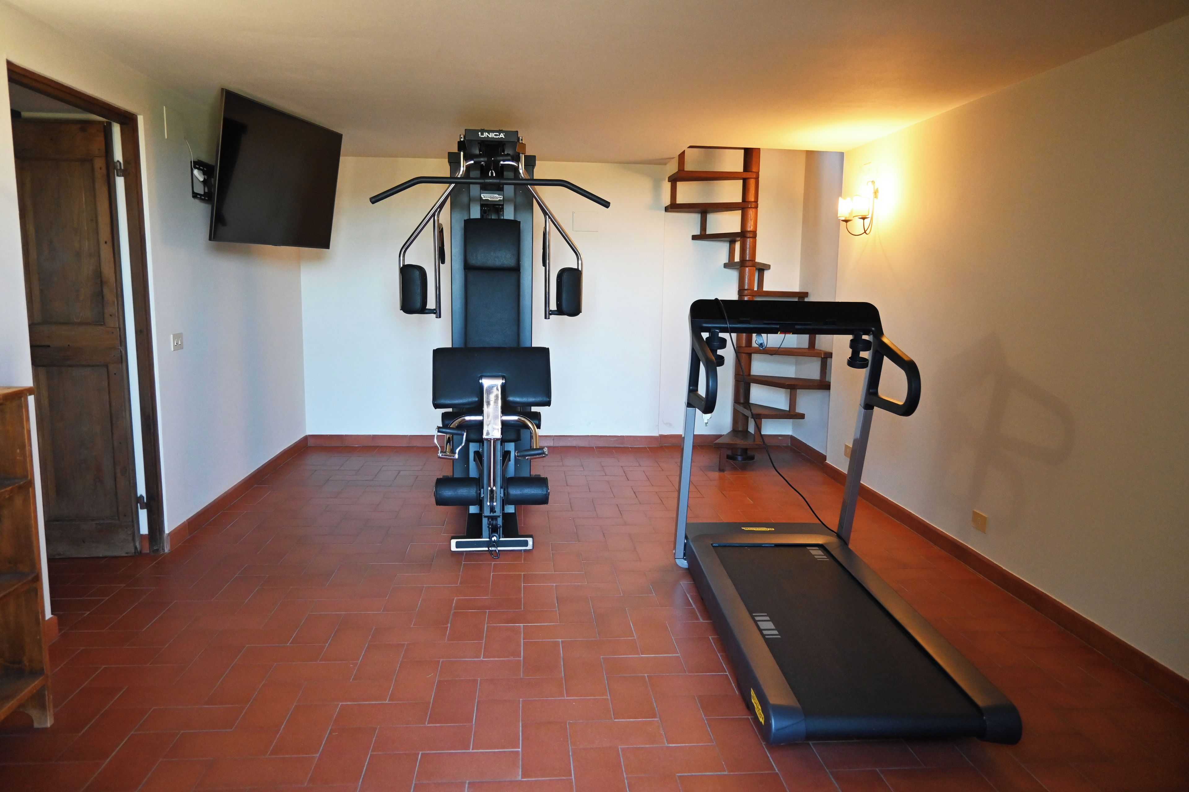 A home gym with a treadmill, weight machine, and a TV mounted on the wall.