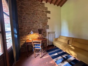A cozy room with a stone wall, a wooden desk with a lamp, a chair, a radiator, and a sofa. - Private Tuscan Wine Estate with 3 Houses and Sweeping Views of the Chianti Hills (Toscana)