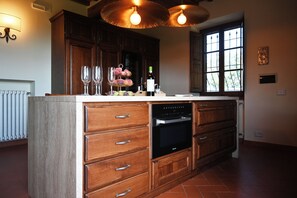 A kitchen with wooden cabinetry, a built-in oven, and a large window. - Private Tuscan Wine Estate with 3 Houses and Sweeping Views of the Chianti Hills (Toscana)