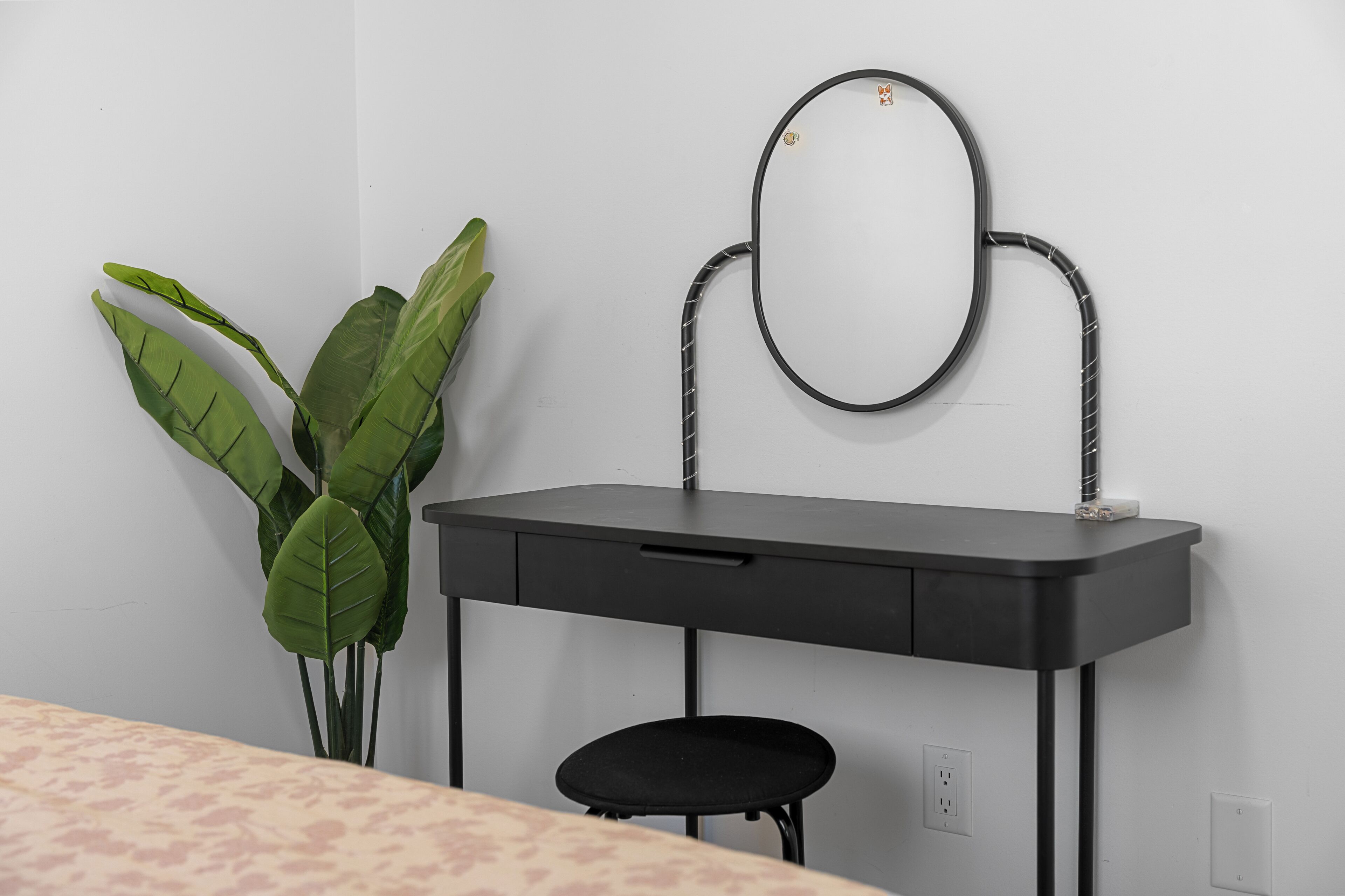 Une pièce avec un bureau noir, un miroir et une plante en pot.