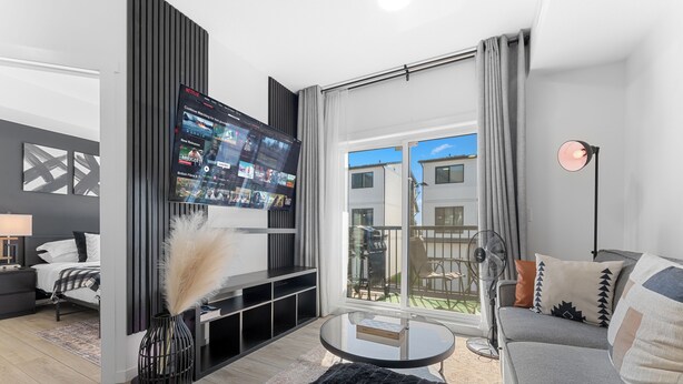 Una sala de estar moderna con un televisor de pantalla plana, un sofá, una mesa de centro y vistas al exterior.