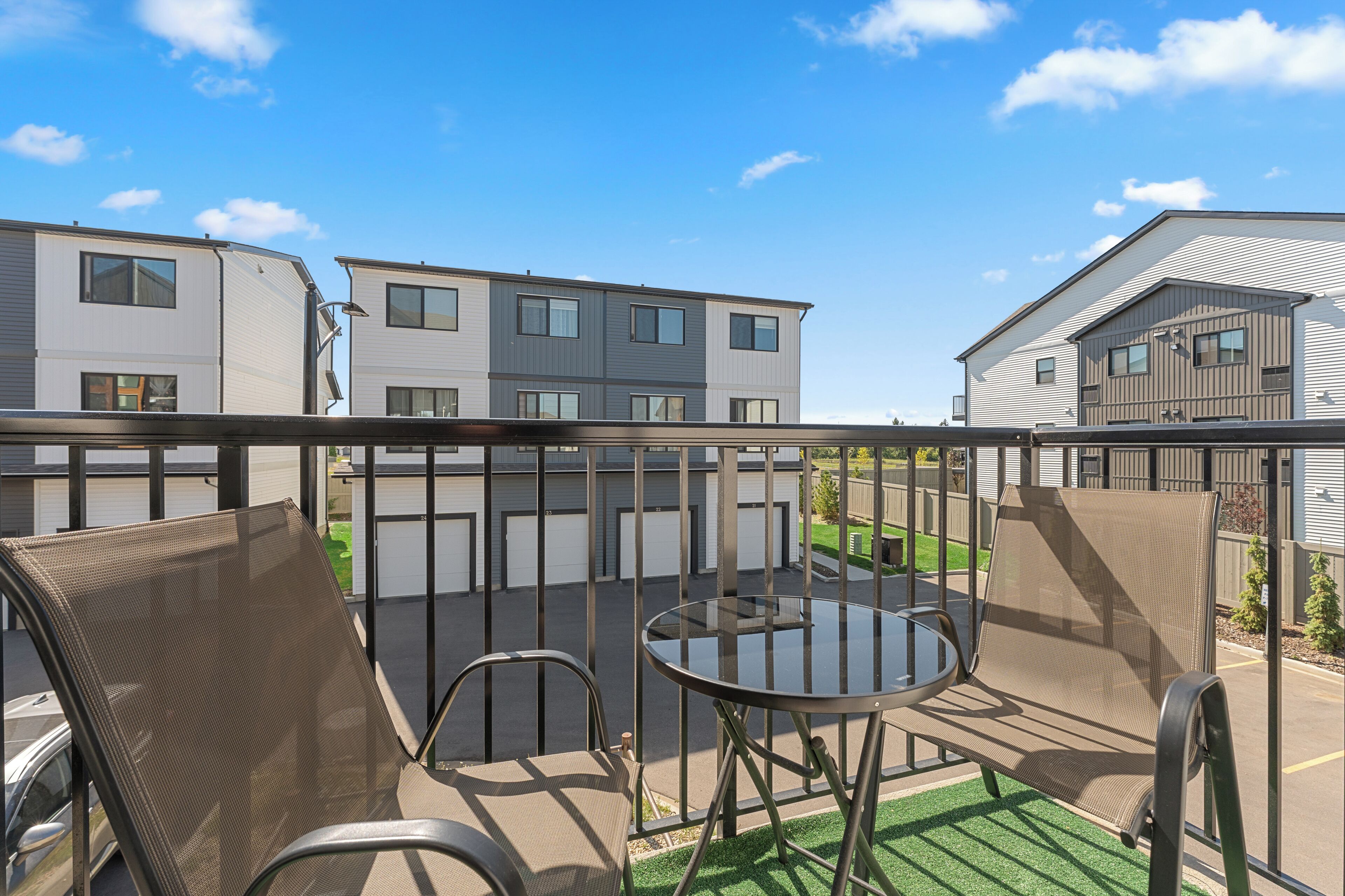 Un balcon aménagé avec du mobilier d’extérieur, une table en verre et une vue sur des immeubles modernes.